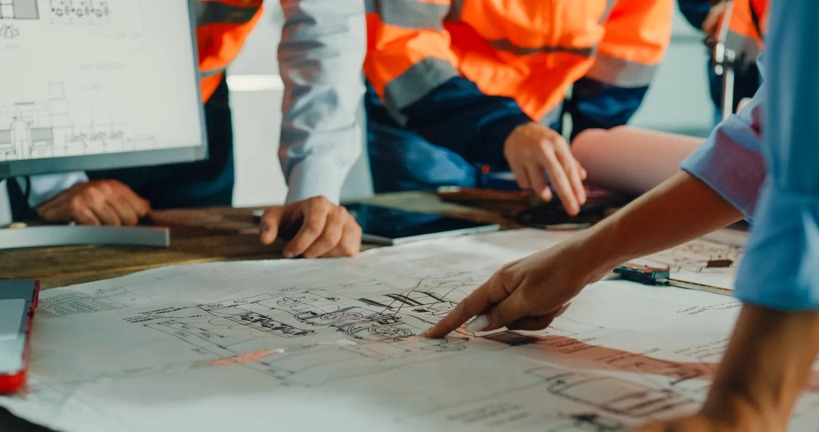 Project team leaning over printed construction drawings, marking up details by hand