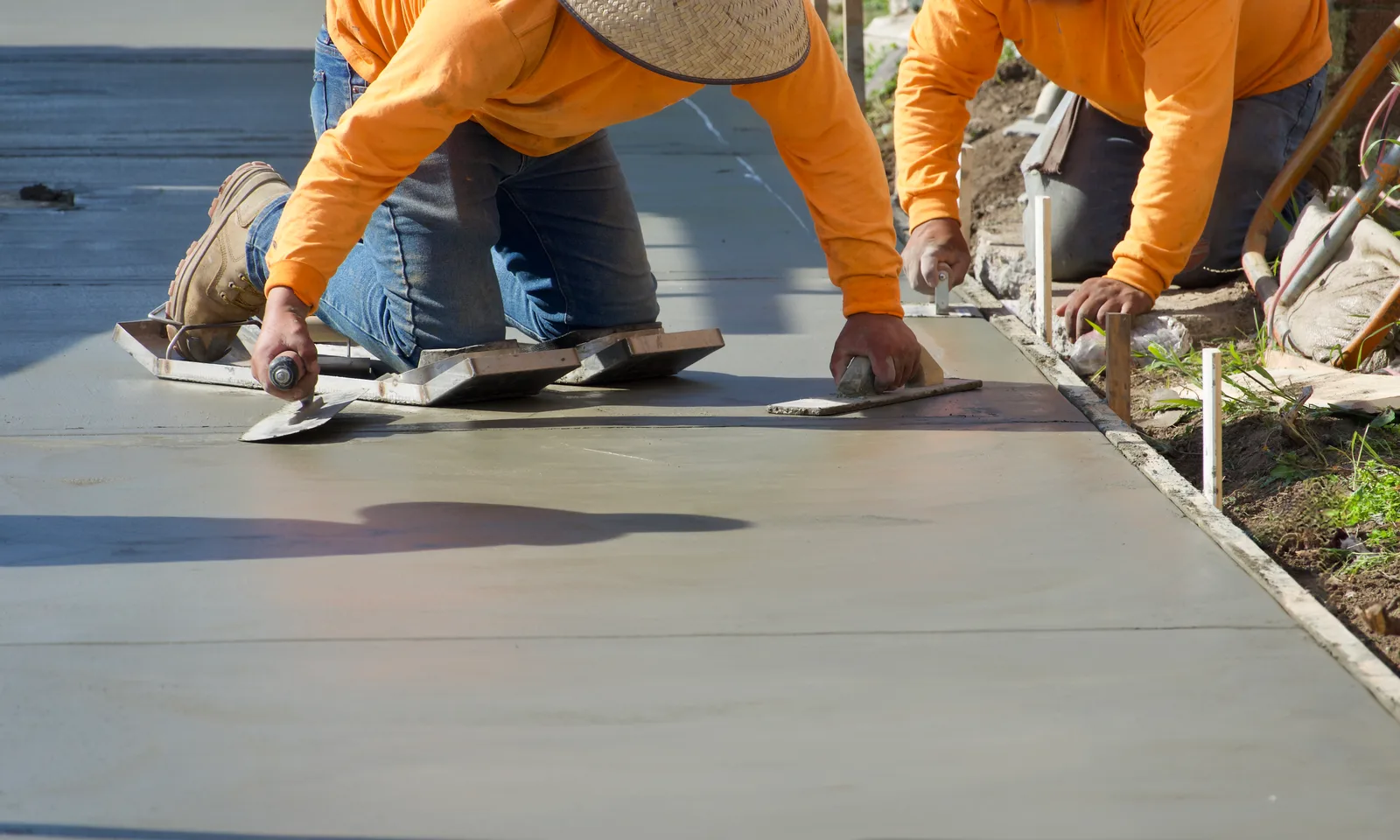 Two concrete finishers in orange shirts kneeling to edge a freshly poured slab