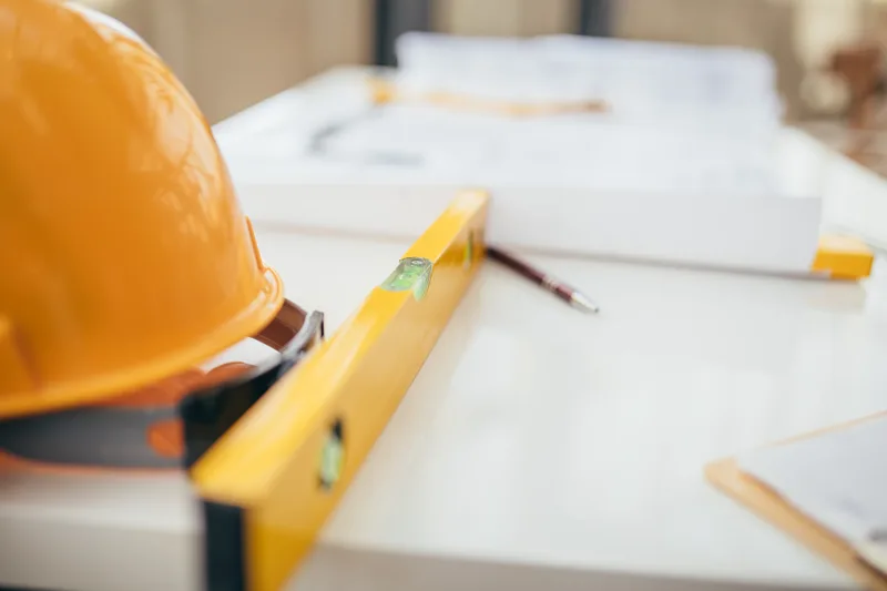 Hard hat, spirit level and rolled drawings on a site office table