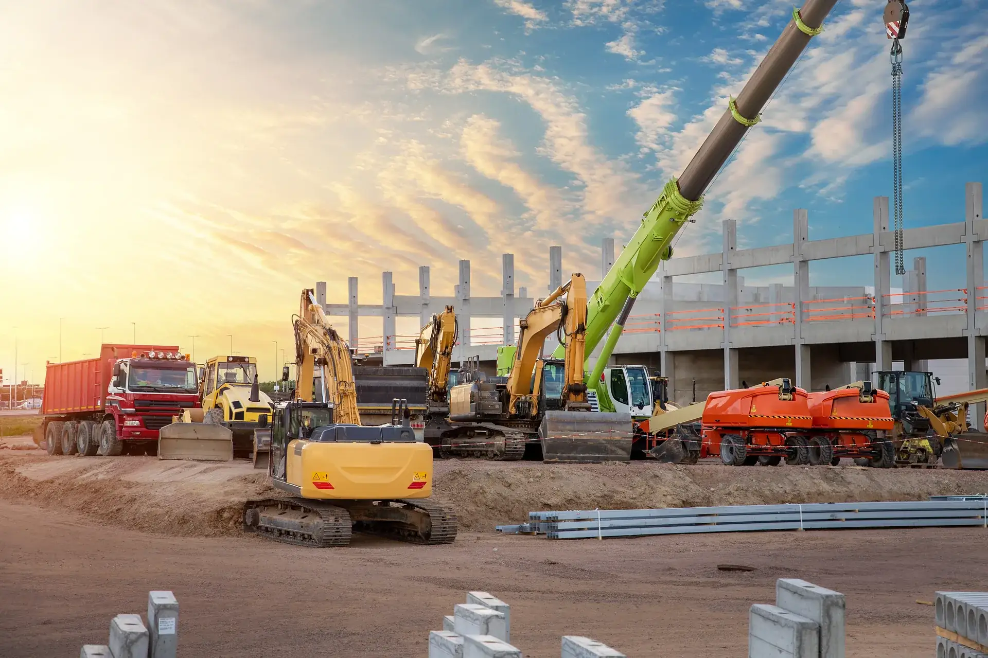 Excavators, haul trucks and a mobile crane staged in front of a precast concrete structure at sunrise on an active construction site