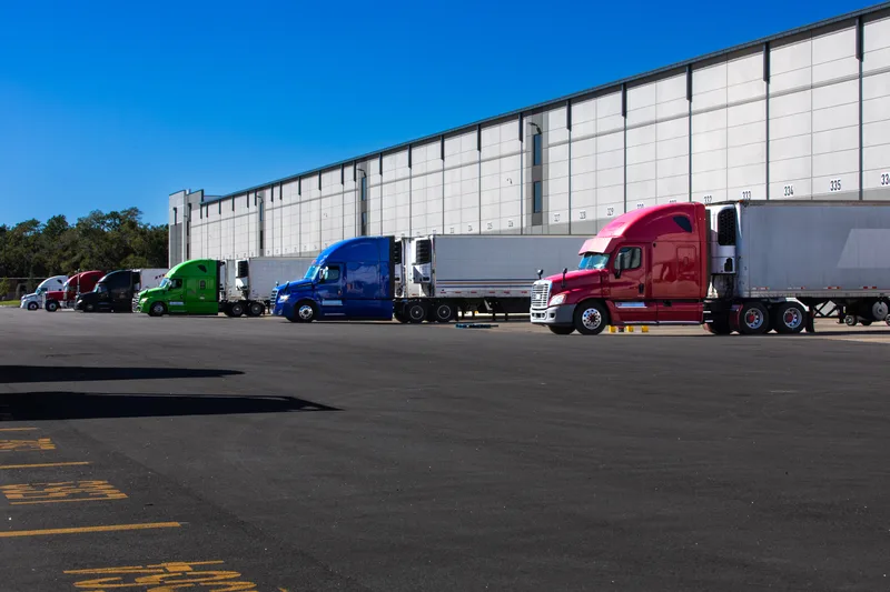 Long distribution warehouse with tractor-trailers parked along its loading docks under a blue sky