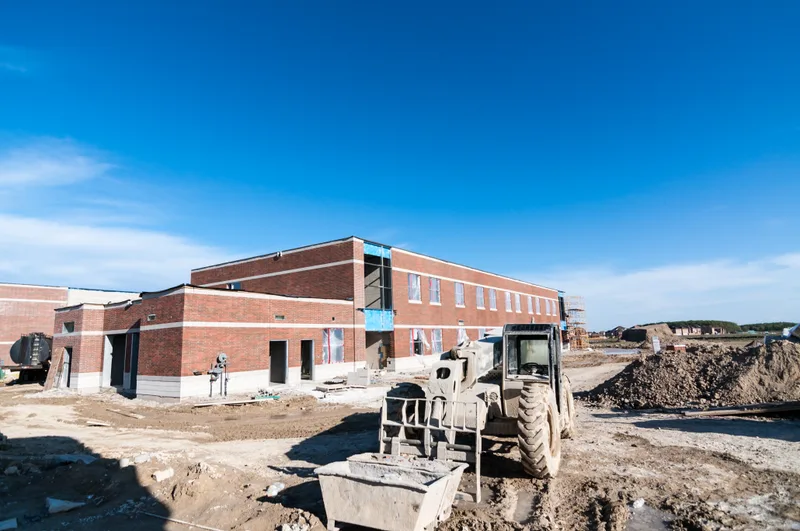 Brick school building nearing completion, with a compact loader working on the graded site in front