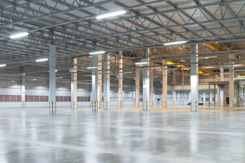 Empty high-bay factory hall with a steel roof structure, rows of columns and a polished concrete floor