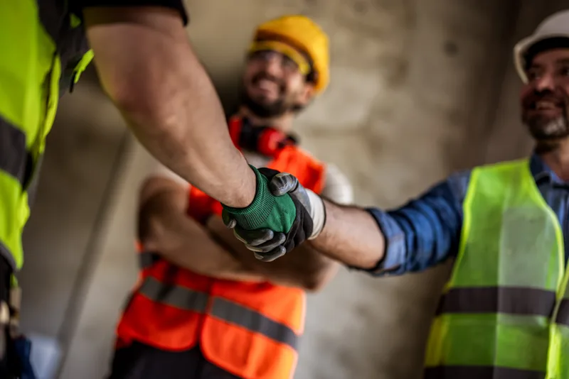 Two construction workers in hard hats and high-visibility vests shaking hands on site