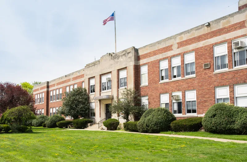 Two-storey red brick school building with a flagpole and a mown front lawn