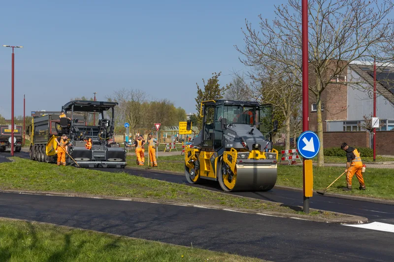 Paver, roller and crew paving a path beside a grass boulevard