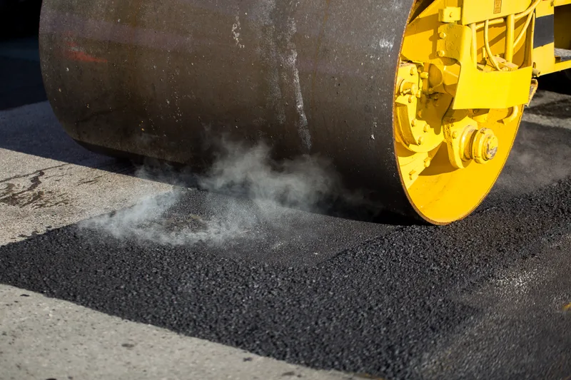 Steel drum of a yellow roller pressing fresh, steaming asphalt flat