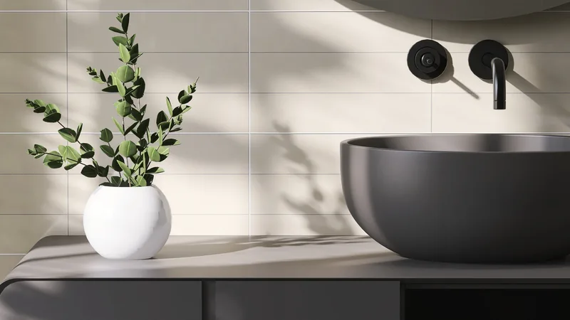 Charcoal stone vessel sink on a slim dark counter with a matte black wall faucet and a small potted plant