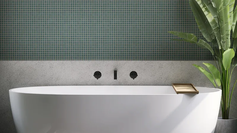 Freestanding white tub against a wall of small green mosaic tile with matte black wall-mounted fixtures