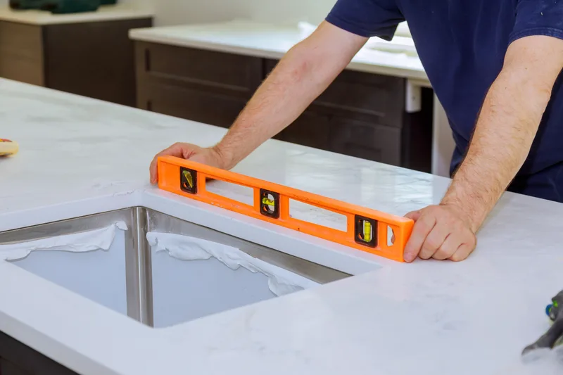 Installer checking a new white quartz countertop with an orange level beside an undermount stainless sink
