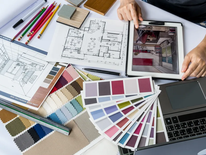 Designer's table with floor plans, a tablet rendering, color fans, fabric swatches, and tile samples
