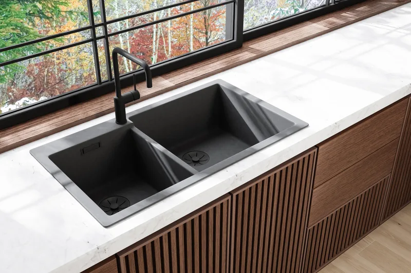 Black composite double sink set into a white quartz counter above a walnut slatted cabinet run, with a window to the trees
