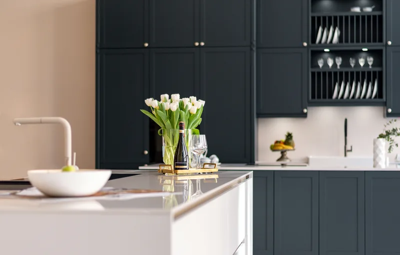 Showroom kitchen display with deep navy shaker cabinets, a white quartz island, and a vase of white tulips
