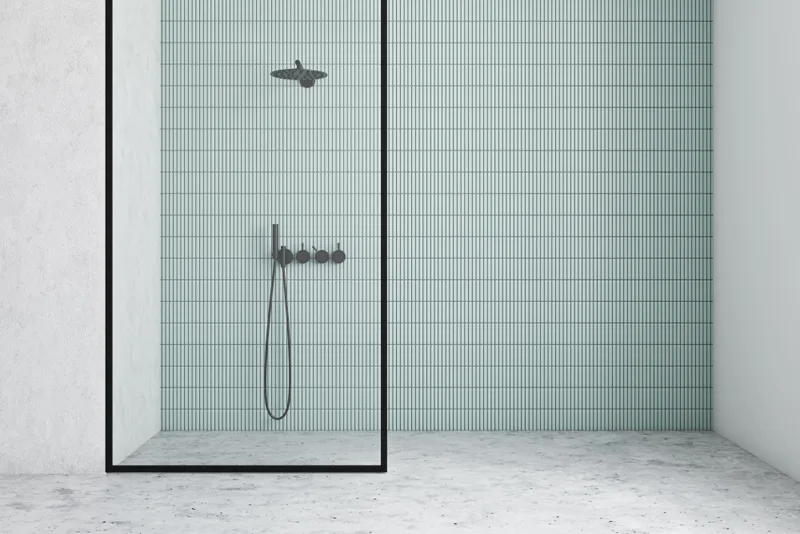 Low-threshold walk-in shower in a former tub alcove, lined with pale green stacked tile and a black-framed glass panel