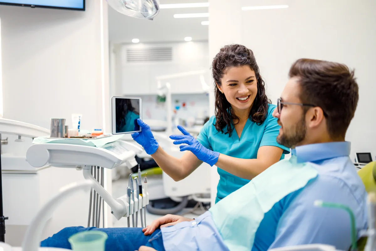 A dentist showing a seated patient his tooth photos on a tablet before treatment begins