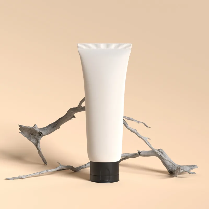 White tube of Quiet Cream with a black cap standing upright in front of a pale driftwood branch on a warm beige ground