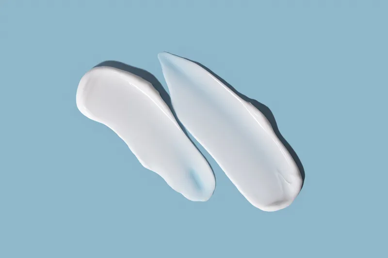 Two smooth swipes of white gel-cream on a dusty blue background