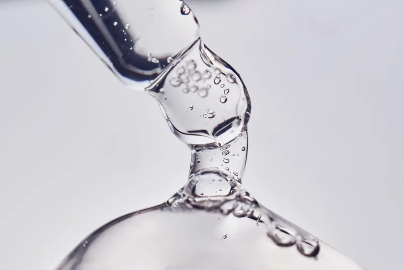 A glass pipette releasing a clear, bubbly serum gel against a pale grey background
