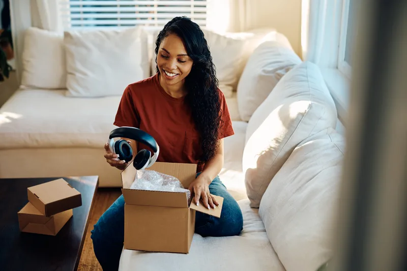 A smiling customer unboxing a new pair of over-ear headphones on her living-room sofa