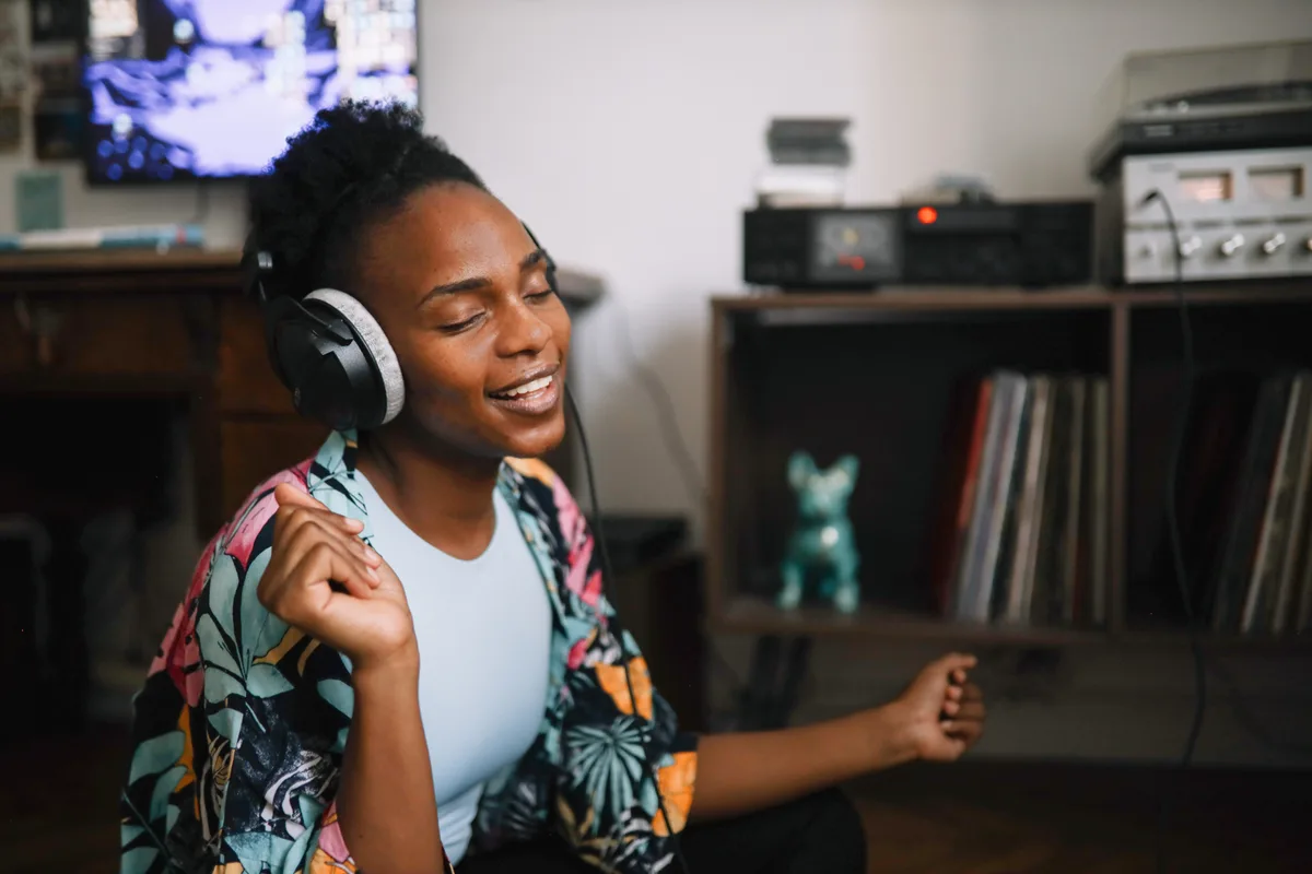 A listener enjoying music on wired over-ear headphones at home beside a turntable and shelf of records