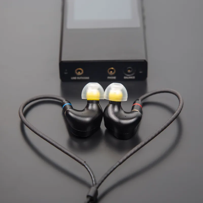 Wrenfield W4 in-ear monitors with a braided cable arranged in front of a portable hi-res audio player