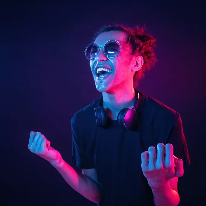 A listener grinning mid-song under pink and blue light, headphones resting around his neck
