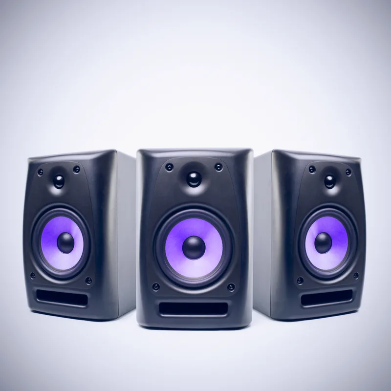 Three compact studio monitors with violet drivers arranged in a row against a white background