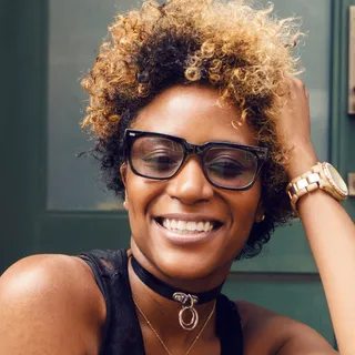 Portrait of Ines Baptiste, a laughing woman with curly hair and dark-framed glasses