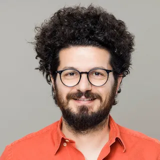 Portrait of Noah Feld, a smiling man with curly hair, a beard and round glasses