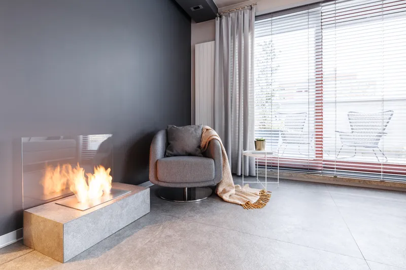 Cozy living room corner with an armchair, a knit throw, and a low fire burning in a modern fireplace