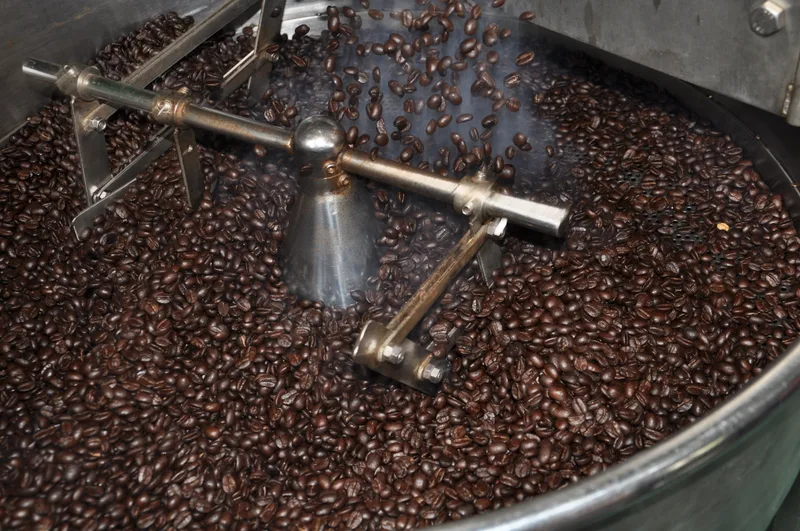 Freshly roasted coffee beans turning in a drum roaster's cooling tray, the stirring arms moving through them