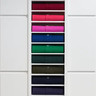 White wardrobe shelves stacked with folded merino crewneck sweaters in cranberry, fuchsia, cobalt, emerald, pine, olive, navy, and ink