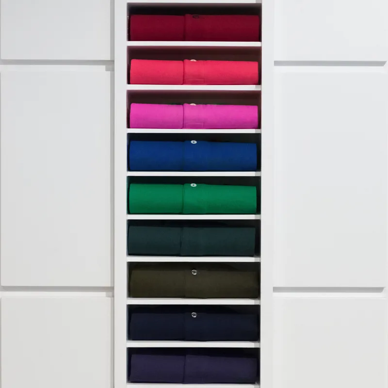 Wardrobe shelves stacked with folded merino sweaters in cranberry, fuchsia, cobalt, emerald, pine, olive, navy, and ink