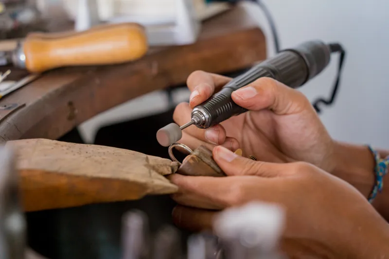 A jeweler's hands at the bench, polishing a gold ring with a rotary tool over a leather catch-skin