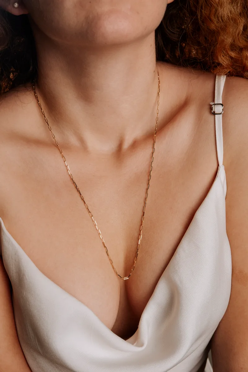 The Fil chain in yellow gold, fine paperclip links falling below the collarbone over an ivory silk slip