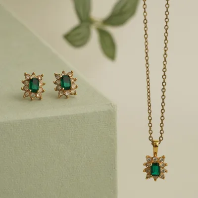 Verte pendant on a gold cable chain — a step-cut emerald surrounded by a starburst halo of small diamonds, beside its matching studs