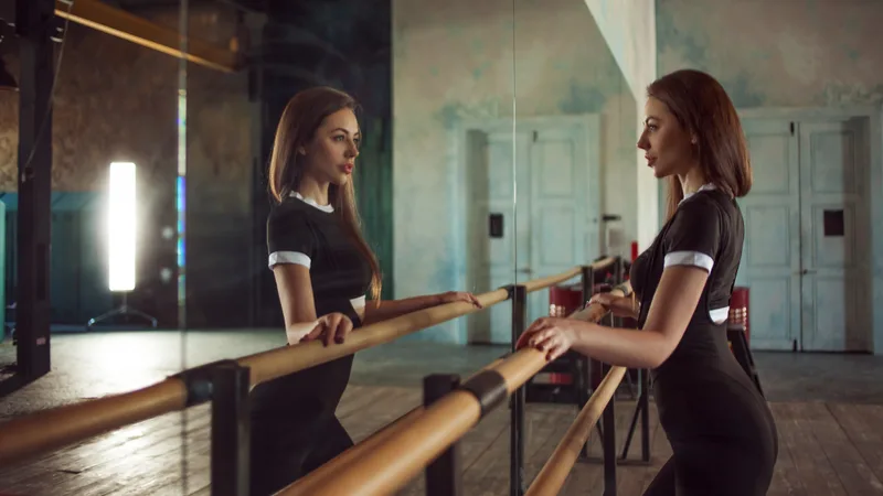 Two dancers at a wooden barre in a studio with tall mirrors