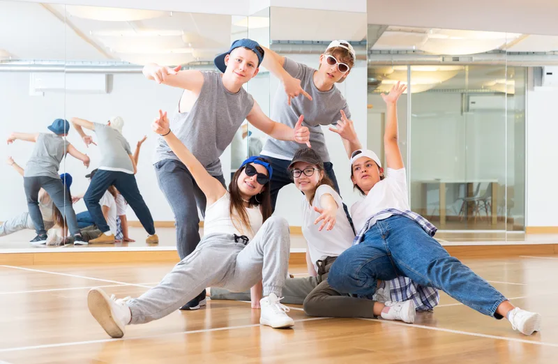 A crew of teenage hip hop dancers in caps and sneakers striking a pose on a studio floor