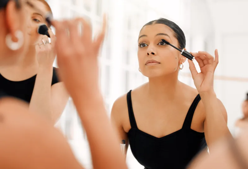 Older dancers in black leotards putting on stage makeup in front of a mirror