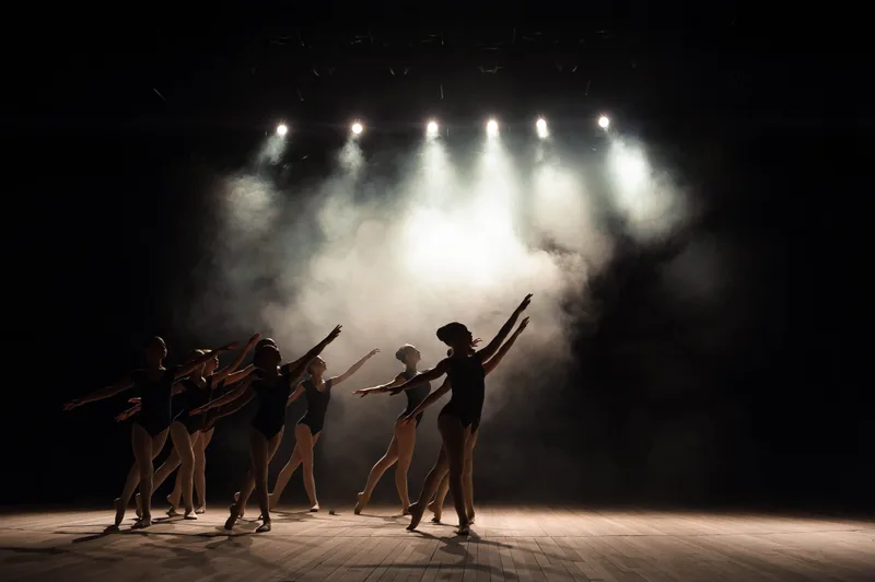 Silhouettes of dancers on a stage under bright stage lights and haze