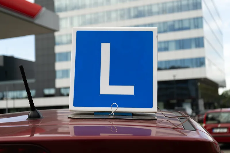 Learner roof sign mounted on a driving school car, city buildings in the background
