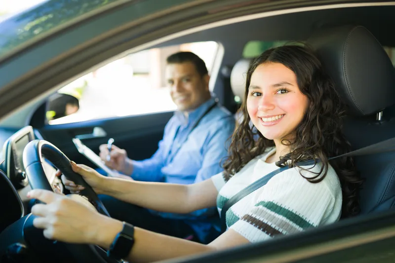 Smiling teenage student behind the wheel while her instructor takes notes on a clipboard