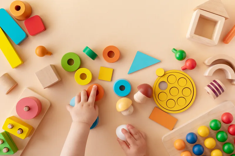 A small hand reaching for colourful wooden stacking toys