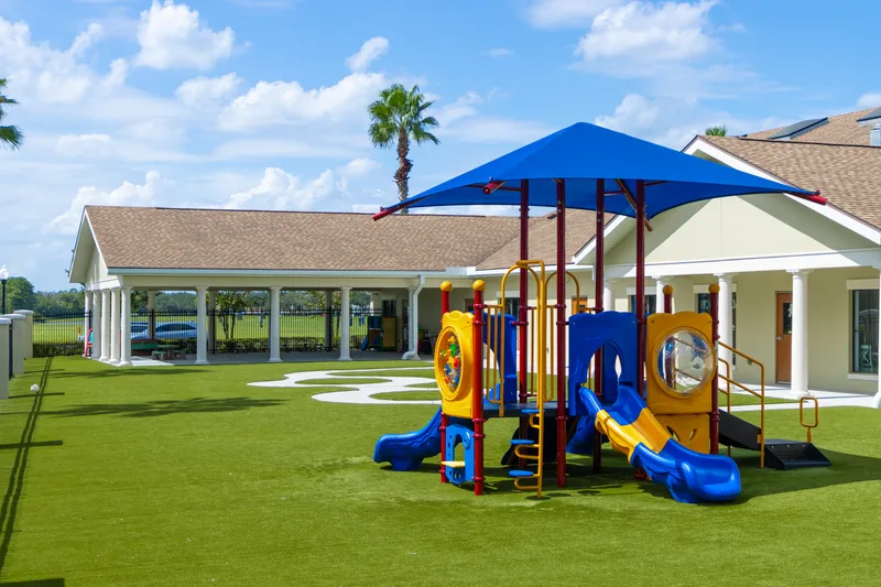 An outdoor play structure with slides under a shade canopy on soft turf