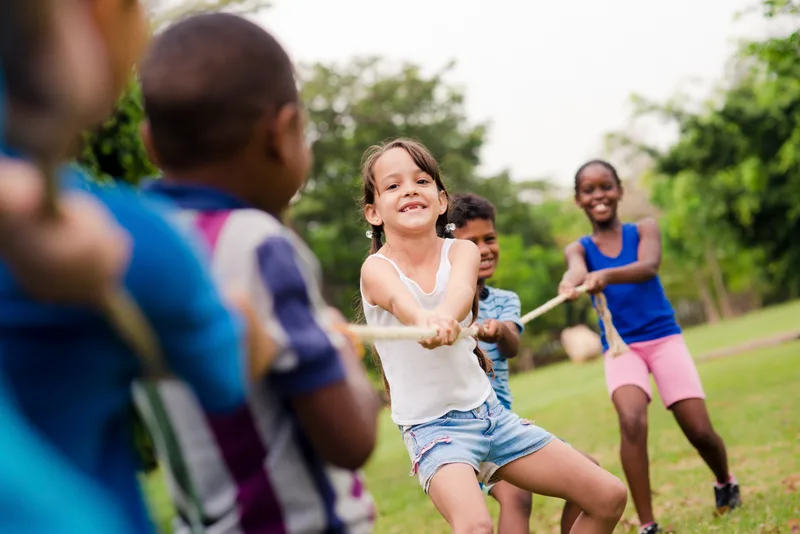 School-age children play tug of war on a grassy field