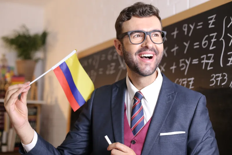 World-languages chair Tomás Herrera laughs while holding a small Colombian flag beside a chalkboard of equations