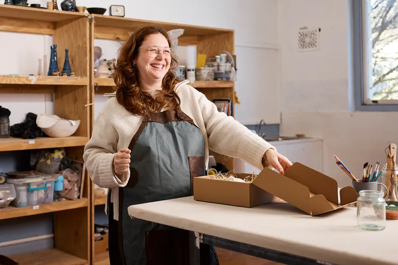 Hattie Brennan laughing in the studio beside an open shipping box