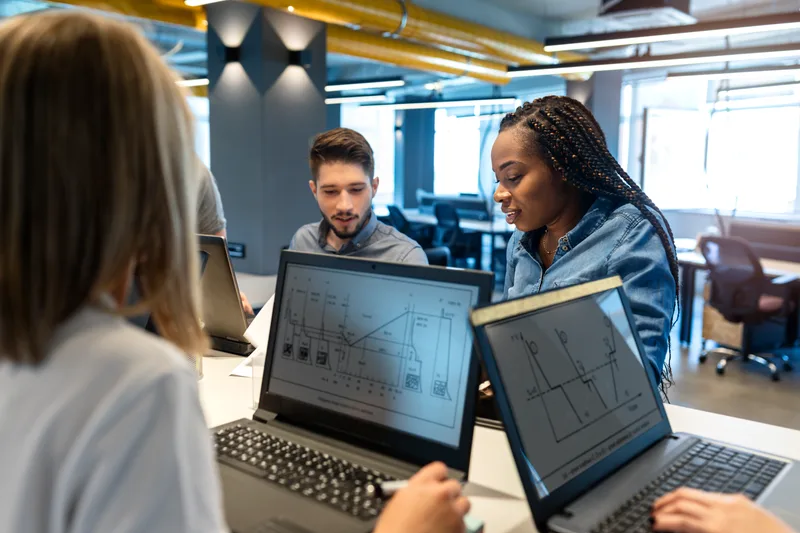 Two students pair-working through wireframe diagrams on their laptop screens in a shared workspace