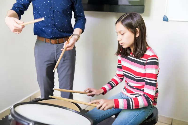 Drum teacher demonstrating stick technique to a young student seated at a drum