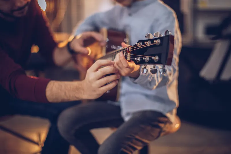 Guitar teacher helping a young student place fingers on the fretboard of an acoustic guitar